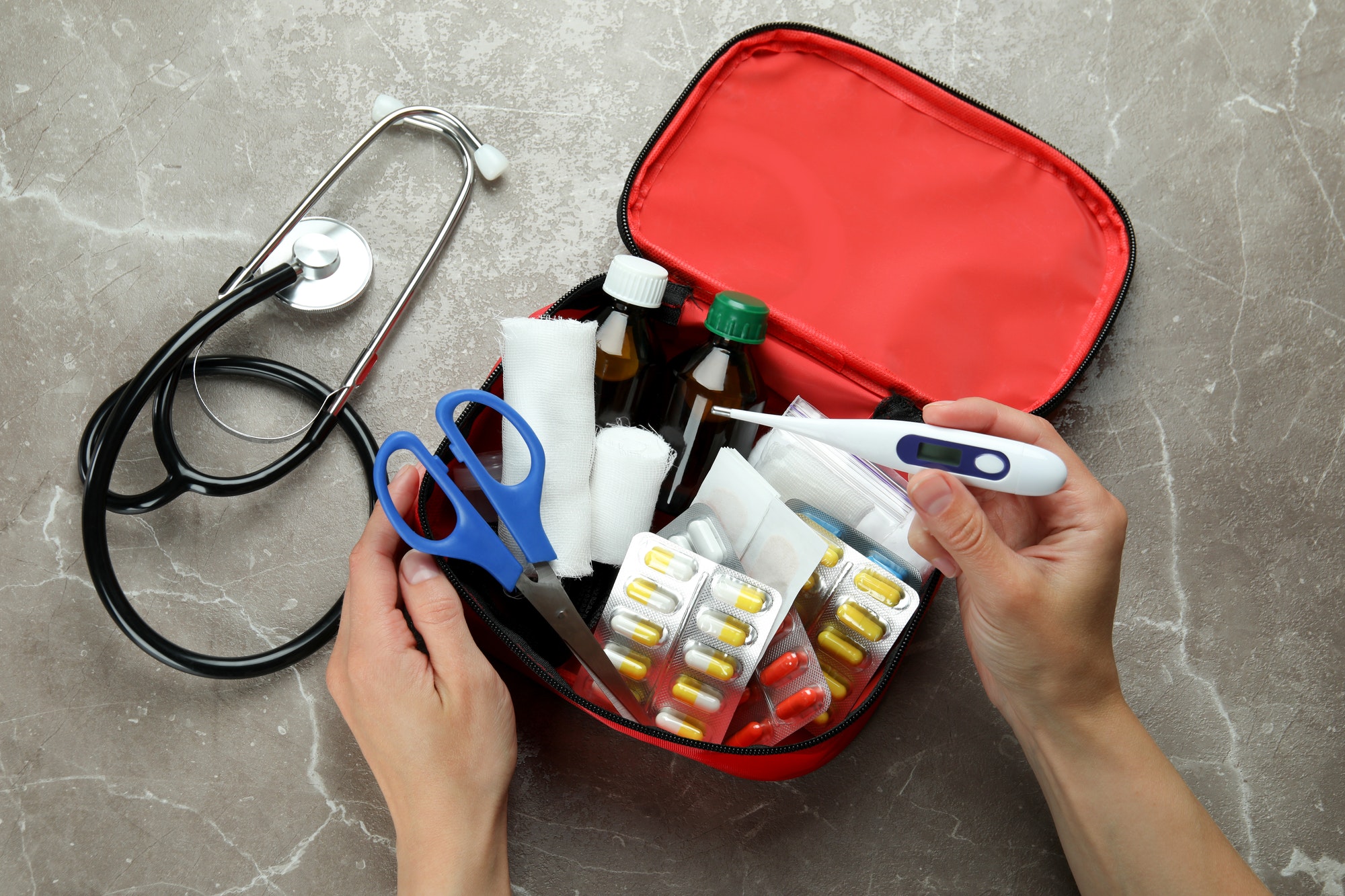 Female hands and first aid medical kit on gray textured background